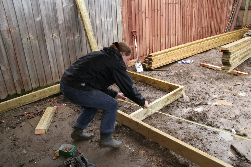 A builder measuring a new timber frame laid out in a backyard