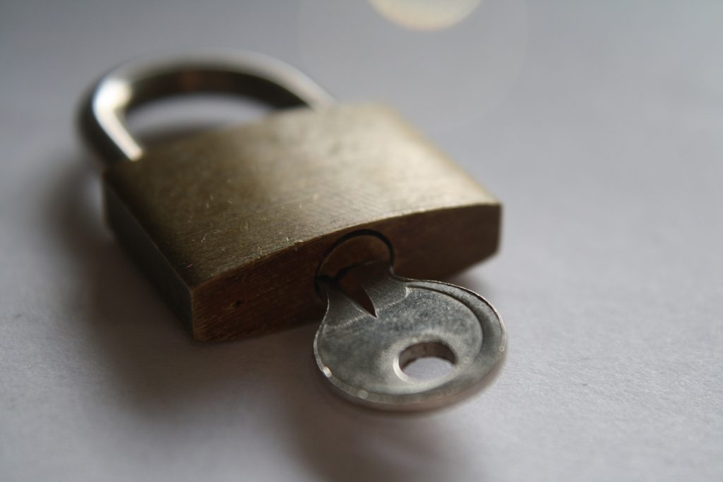 A brass padlock with its key in the lock resting on a pale surface